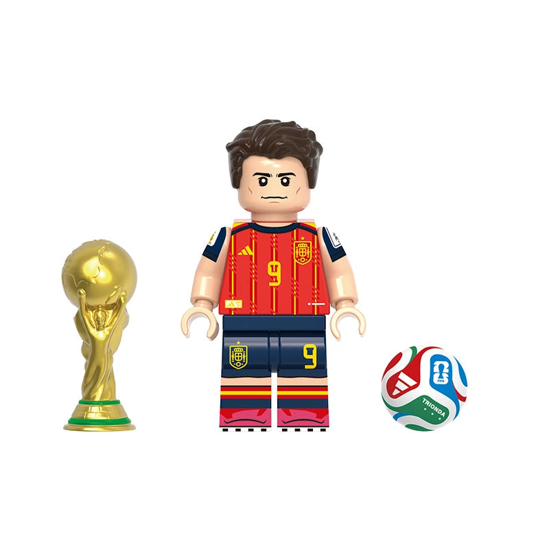 A toy soccer minifigure named Gavi shown on a white background, flanked by a gold FIFA World Cup trophy and a multicolor soccer ball. The figure wears a red Spain jersey with the number 9 and dark blue shorts.