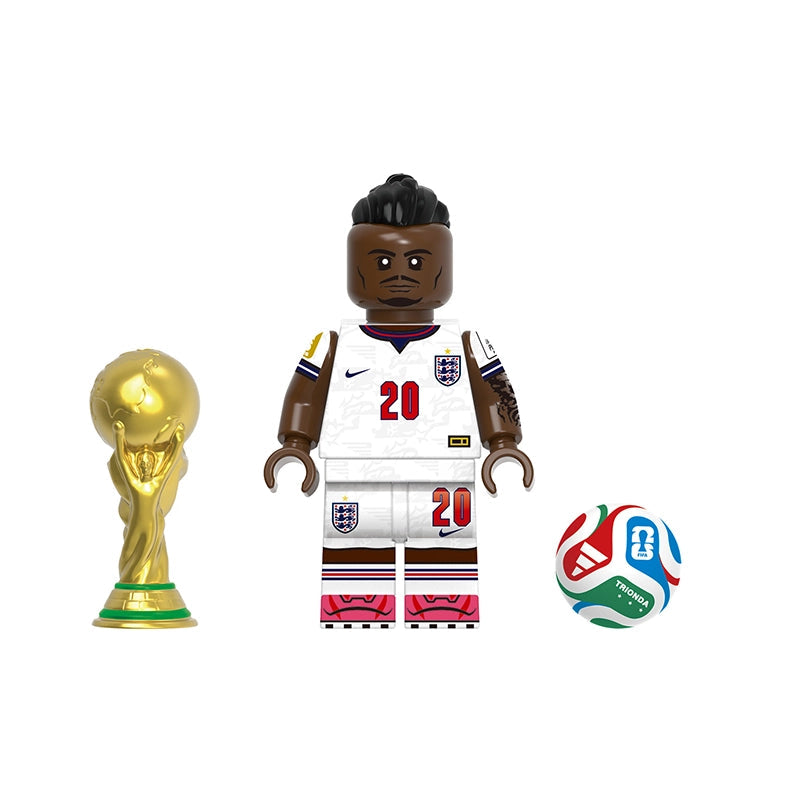 A toy minifigure labeled 'Madueke' shown with a gold FIFA-style trophy and a soccer ball on a plain white background. The figure wears a white England jersey with red number 20 and crest details.