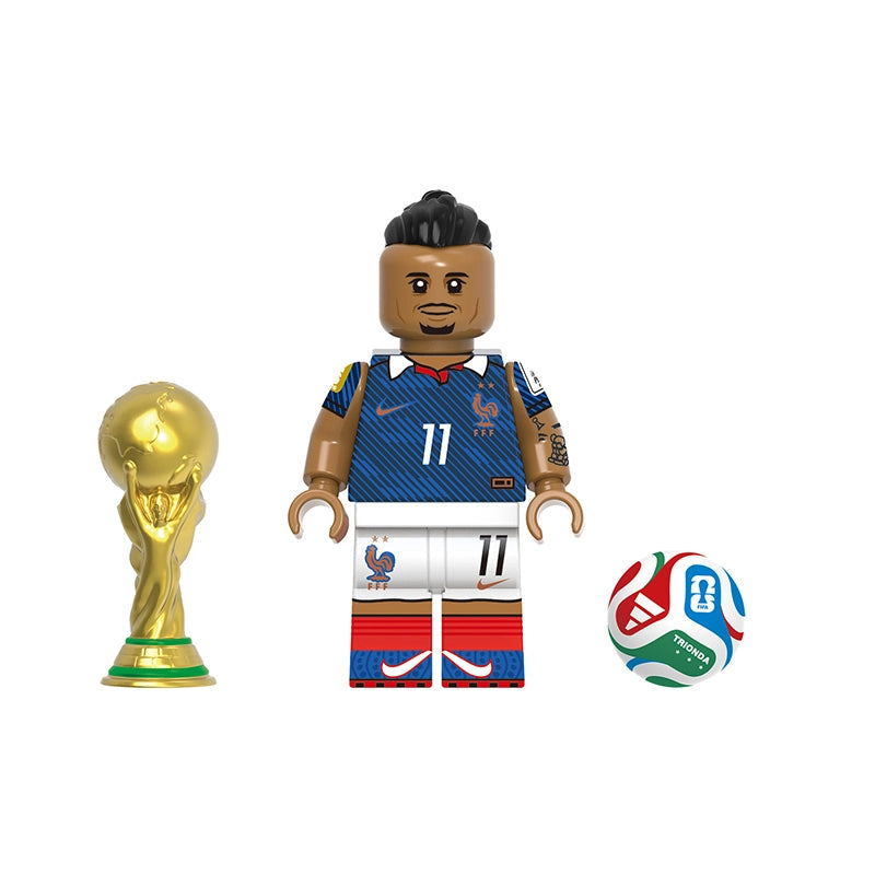 A toy soccer minifigure named Olise with a blue France jersey, white shorts, and red striped socks, shown alongside a gold FIFA trophy and a multicolor soccer ball on a white background.