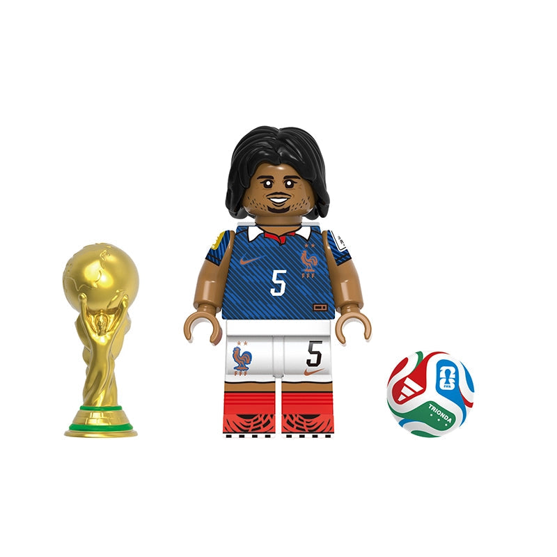 A toy minifigure of Kounde wearing a blue and white France soccer jersey with the number 5, shown with a gold FIFA trophy and a soccer ball on a white background. The text 'Koundé' and 'GH0829' are printed on the image.